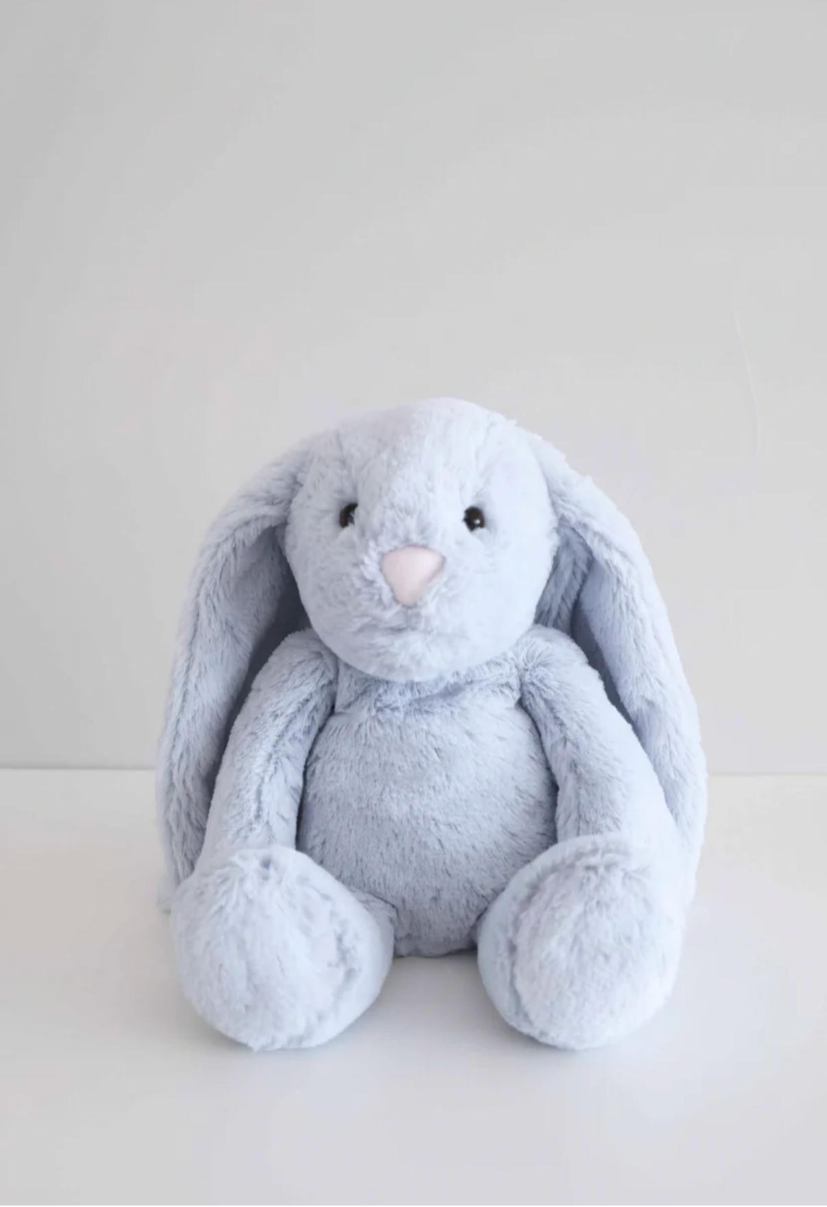 The Caden Lane Large Cuddle Plush Friends | Honey Bunny is a soft, light blue bunny with long floppy ears, sitting upright—an adorable plush toy that makes a perfect newborn gift.