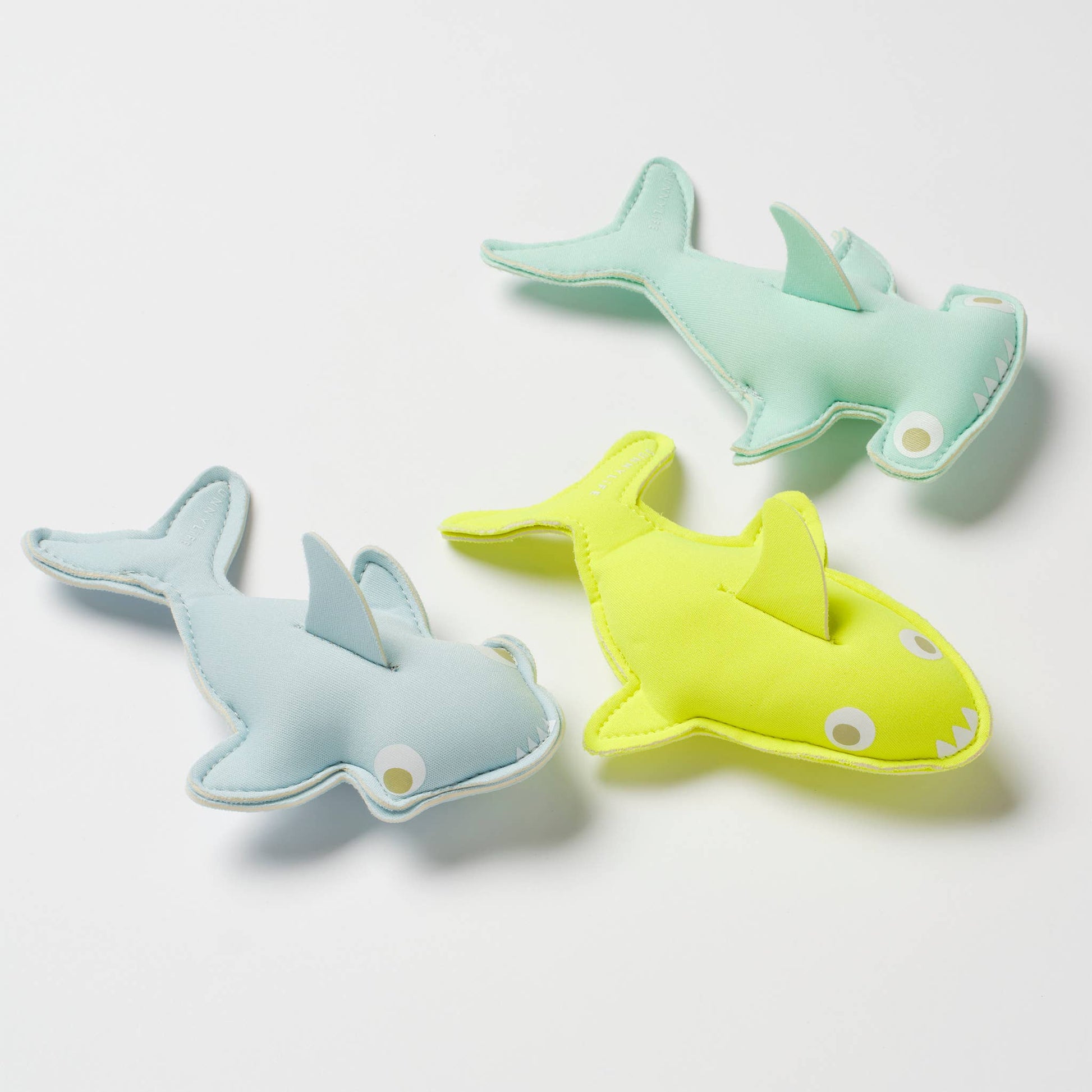 Three shark-shaped toys in green, blue, and yellow on a white background