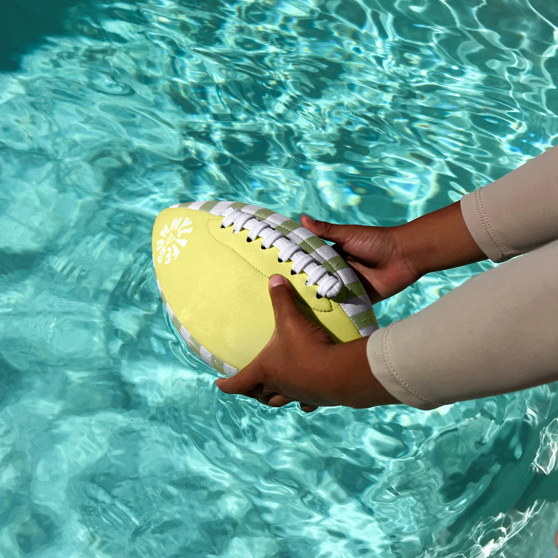 Person holding a yellow and green football by a pool