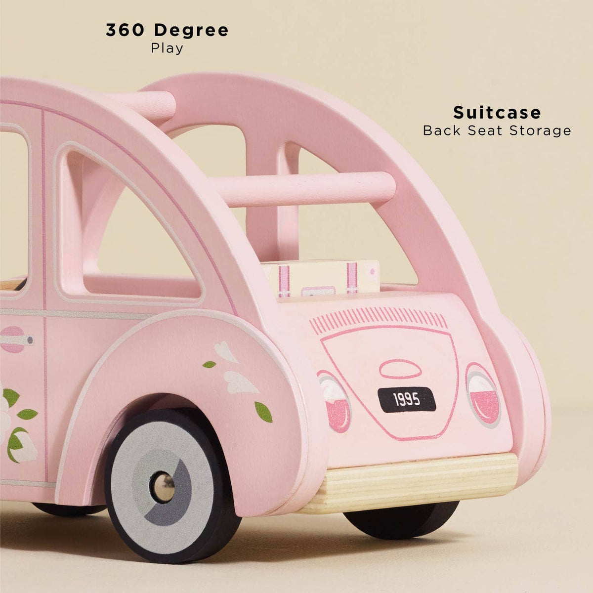The Sophie's Dolls House Toy Car by Le Toy Van, Inc. is a pink wooden car with a floral design and removable suitcase. Enjoy 360-degree play, suitcase back seat storage, retro style, and a fun "1995" license plate—all plastic-free!.