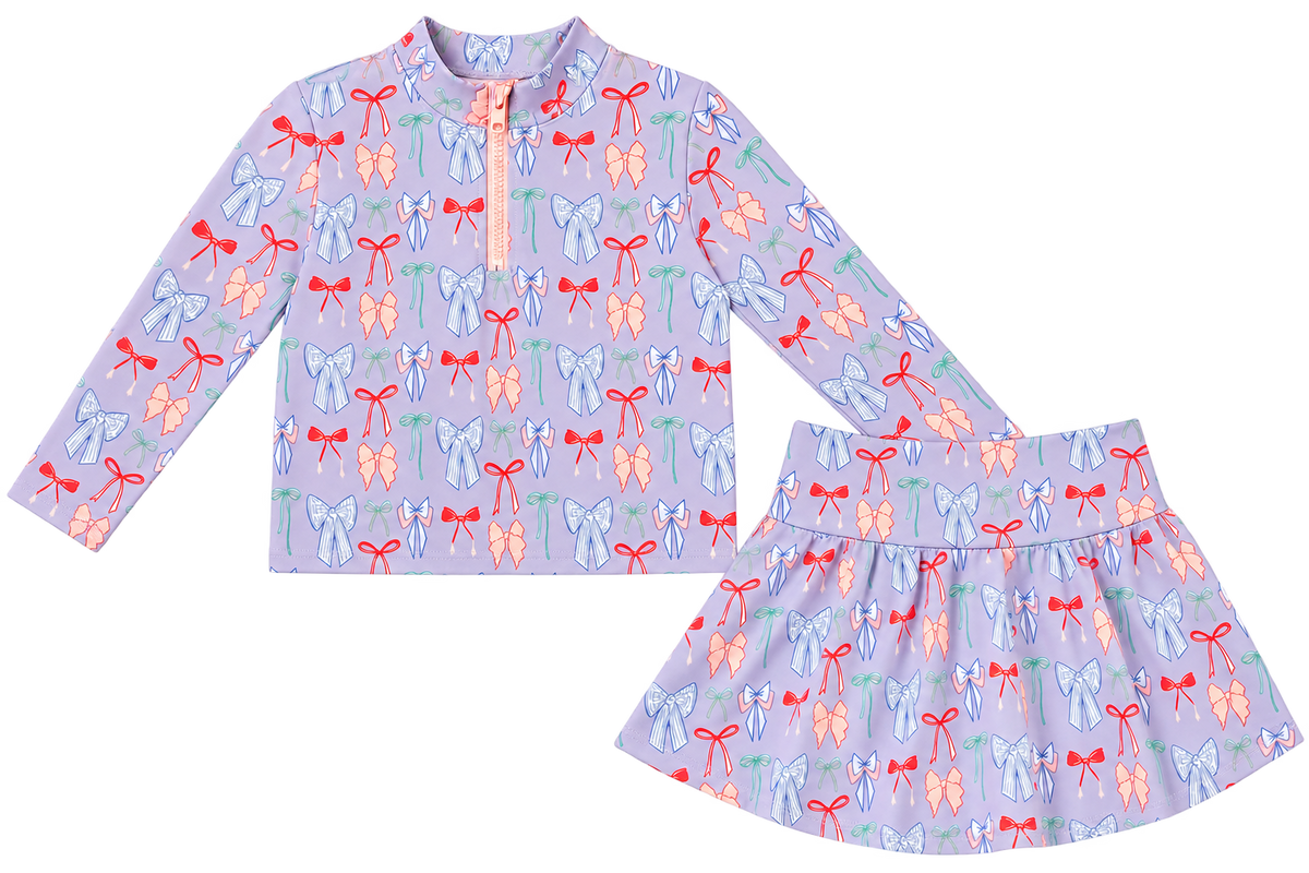 Girls lavender two-piece activewear set with colorful bow print, long-sleeve quarter-zip top and matching skirt.