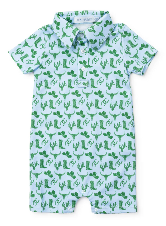 The Lila and Hayes Wildwest Tripp Shortall is a light blue, short-sleeve baby romper with a collar, featuring a green Western-themed print of cowboy hats, boots, cacti, and horseshoes.