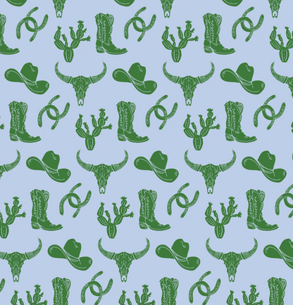 The Lila and Hayes Wildwest Tripp Shortall features a seamless pattern of green cowboy hats, boots, longhorn skulls, cacti, and horseshoes on light blue—perfect for a playful touch to any little one’s cowboy or rodeo outfit.