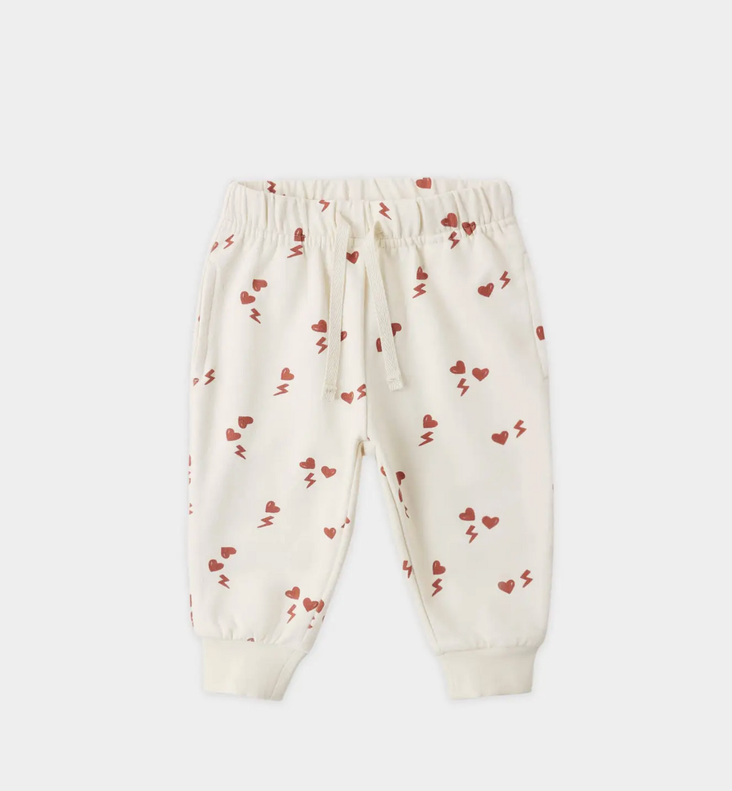 The Quincy Mae Electric Heart Relaxed Sweatpant for toddlers features a cream color, playful red hearts and lightning bolts, an elastic waistband with drawstring, ribbed cuffs, and is made from organic cotton for cozy comfort.