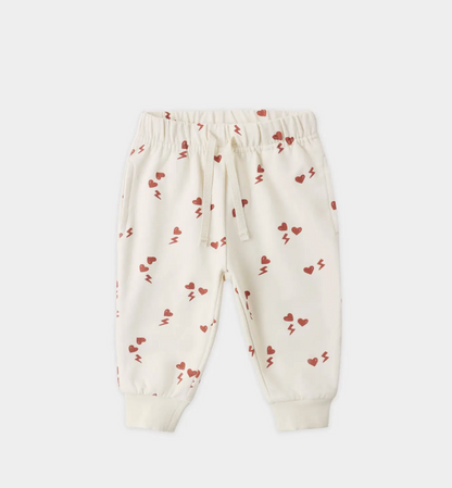 The Quincy Mae Electric Heart Relaxed Sweatpant for toddlers features a cream color, playful red hearts and lightning bolts, an elastic waistband with drawstring, ribbed cuffs, and is made from organic cotton for cozy comfort.