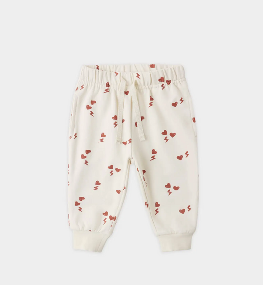 The Quincy Mae Electric Heart Relaxed Sweatpant for toddlers features a cream color, playful red hearts and lightning bolts, an elastic waistband with drawstring, ribbed cuffs, and is made from organic cotton for cozy comfort.