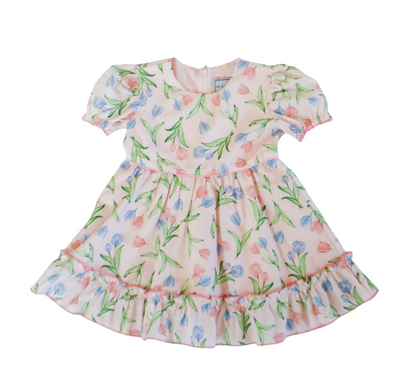 The Hollis Baker Everly Tulips Dress is a light pink, short-sleeved kids' dress with blue and pink tulip prints, green leaves, a round neckline, ruffled hem, and puff sleeves—ideal for spring occasions.