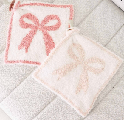 The Caden Lane CuddleLane™ Luxe Lovey | Bows features two soft, square white cloths with fuzzy pink bow designs and corner loops, providing cozy comfort for baby on any surface.