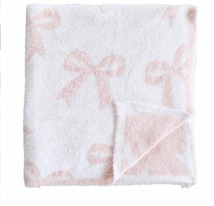 The CuddleLane™ Luxe Blankets | Bows by Caden Lane is a soft, white, square baby blanket featuring light pink bow patterns and a folded corner that reveals the reverse—ideal for stylish nursery décor.
