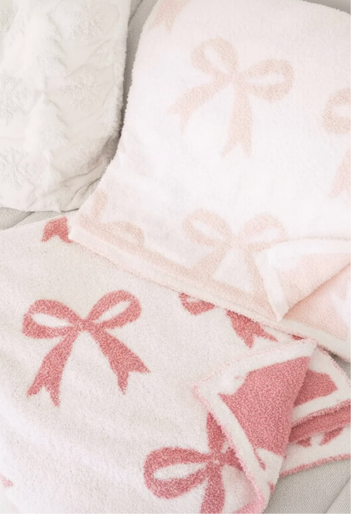 The Caden Lane CuddleLane™ Luxe Blankets | Bows set features a fluffy, soft texture with light and dark pink bow patterns—perfect for nursery décor and adding warmth to any light-colored surface.