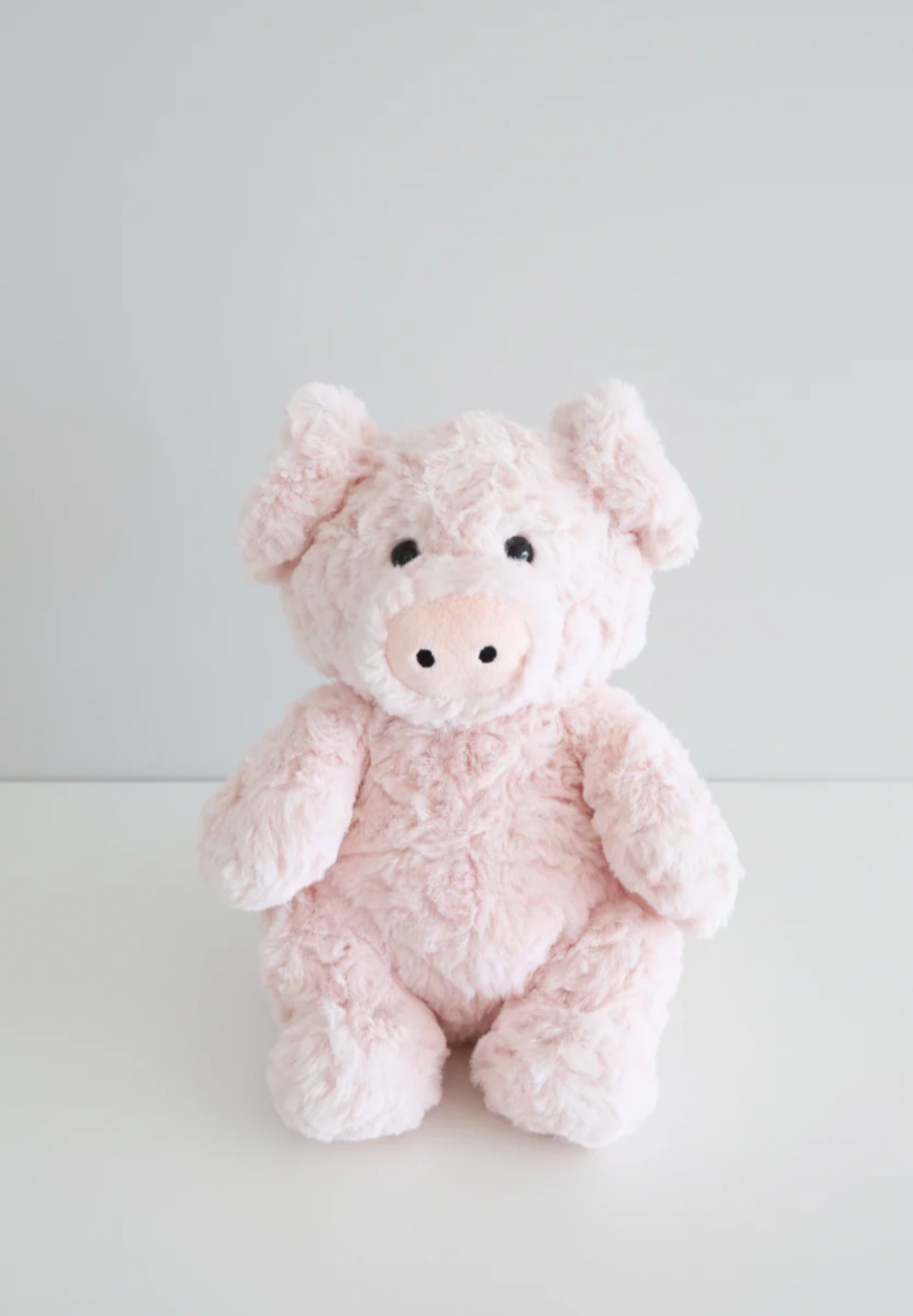 The Caden Lane Large Cuddle Plush Friends | Piper Pig is a soft, light pink plush toy with black eyes and a round snout, sitting upright on a white surface against a plain light gray background.