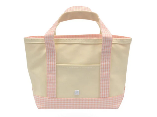 The TRVL Mini Tote by TRVL is an eco-friendly, cream mini tote with light pink gingham handles, a bottom trim, and a front pocket. Its soft pastel look makes it a stylish and simple choice for kids.