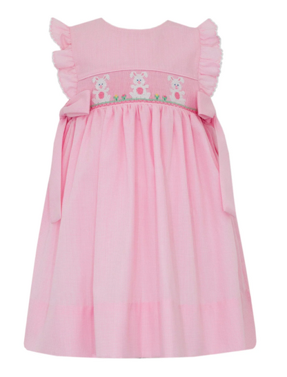 The Petie Bebe Bunnies With Side Bows Dress is a charming pink micro check girls' dress featuring ruffled shoulders, smocked bunnies, green grass embroidery, side bows, and a full gathered skirt—perfect for special occasions.