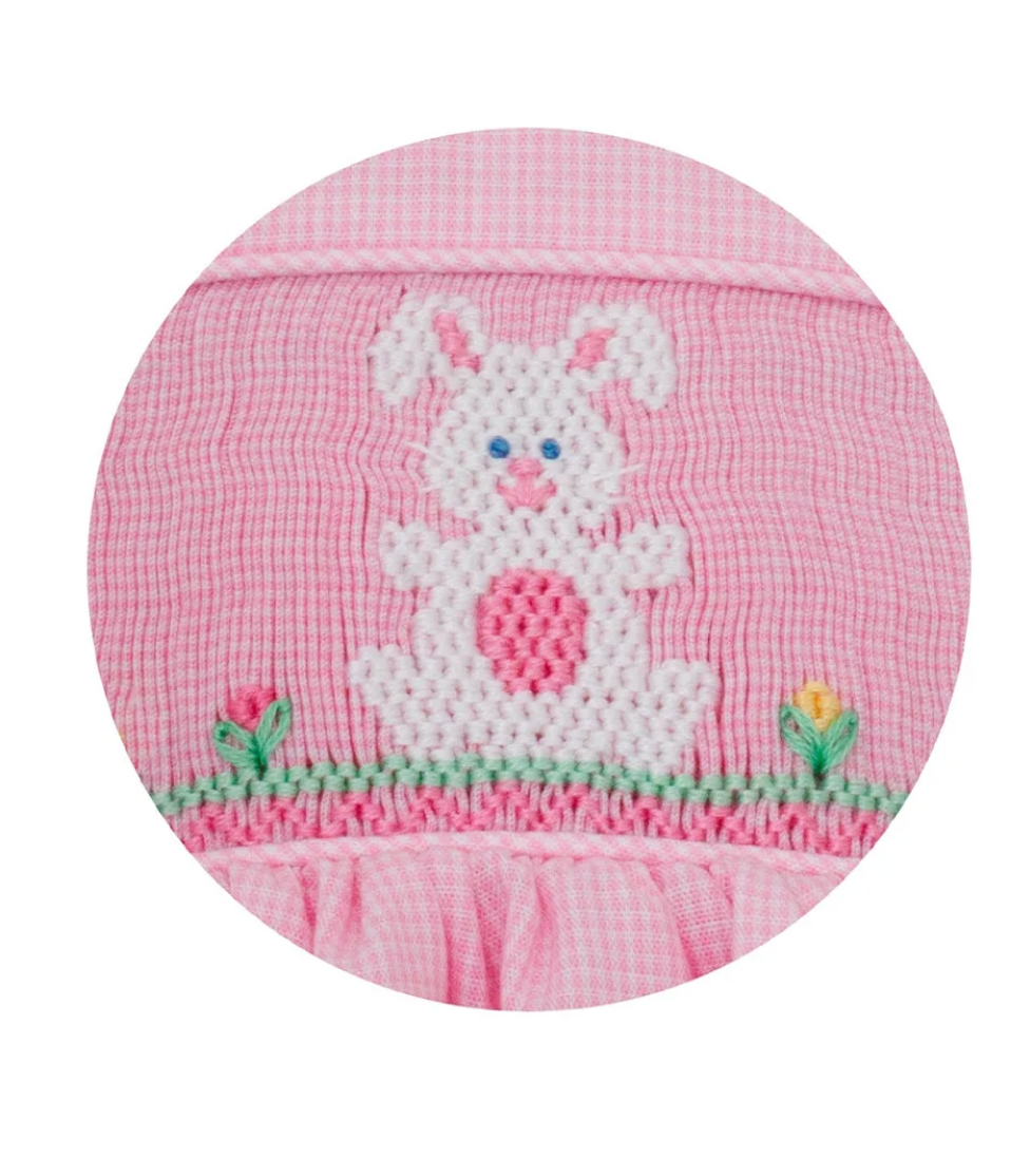 The Bunnies With Side Bows Dress by Petie Bebe features a white, cross-stitched bunny with pink and blue details on green grass with embroidered flowers—perfect for girls’ special occasions.