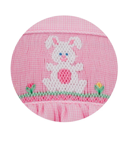 The Bunnies With Side Bows Dress by Petie Bebe features a white, cross-stitched bunny with pink and blue details on green grass with embroidered flowers—perfect for girls’ special occasions.