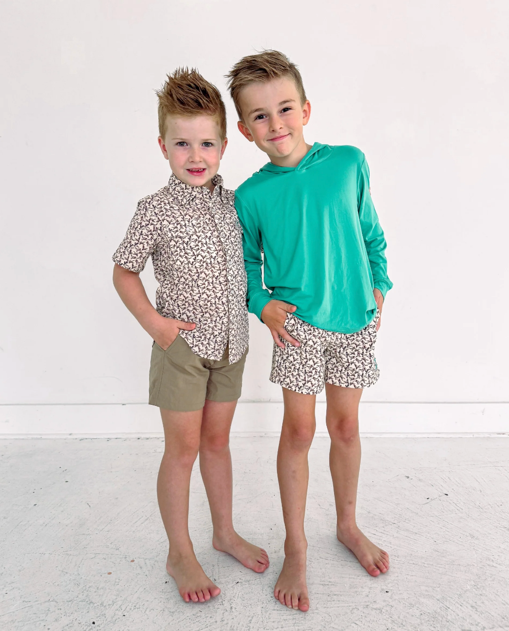 Two young boys wearing matching outfits with floral patterns on a white background