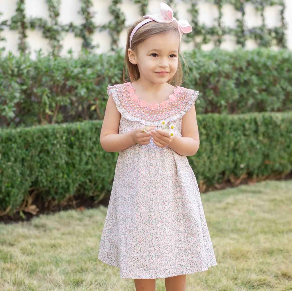 Young girl in a floral dress standing outdoors with greenery in the background