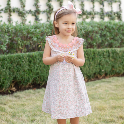 Young girl in a floral dress standing outdoors with greenery in the background