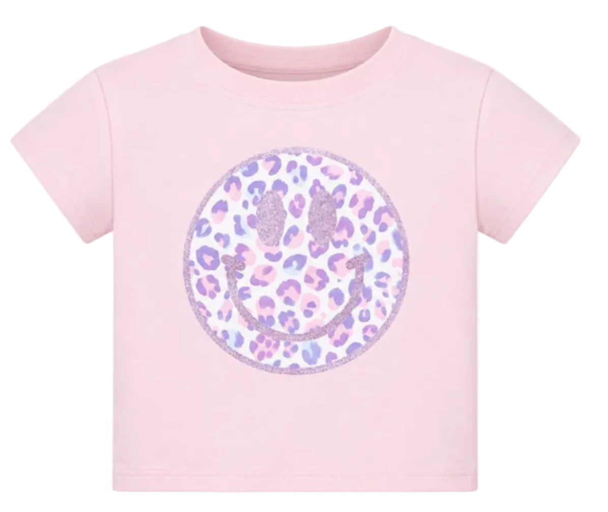 A light pink short-sleeve baby t-shirt featuring a large circular smiley face graphic on the chest. The smiley face is filled with a purple and pink leopard print pattern and outlined with glittery purple details.