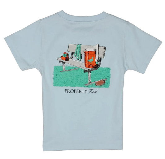 A light blue short-sleeve t-shirt with a vintage-style graphic of a football bench scene and the text 'PROPERLY tied printed on the front, displayed on a clean white background.