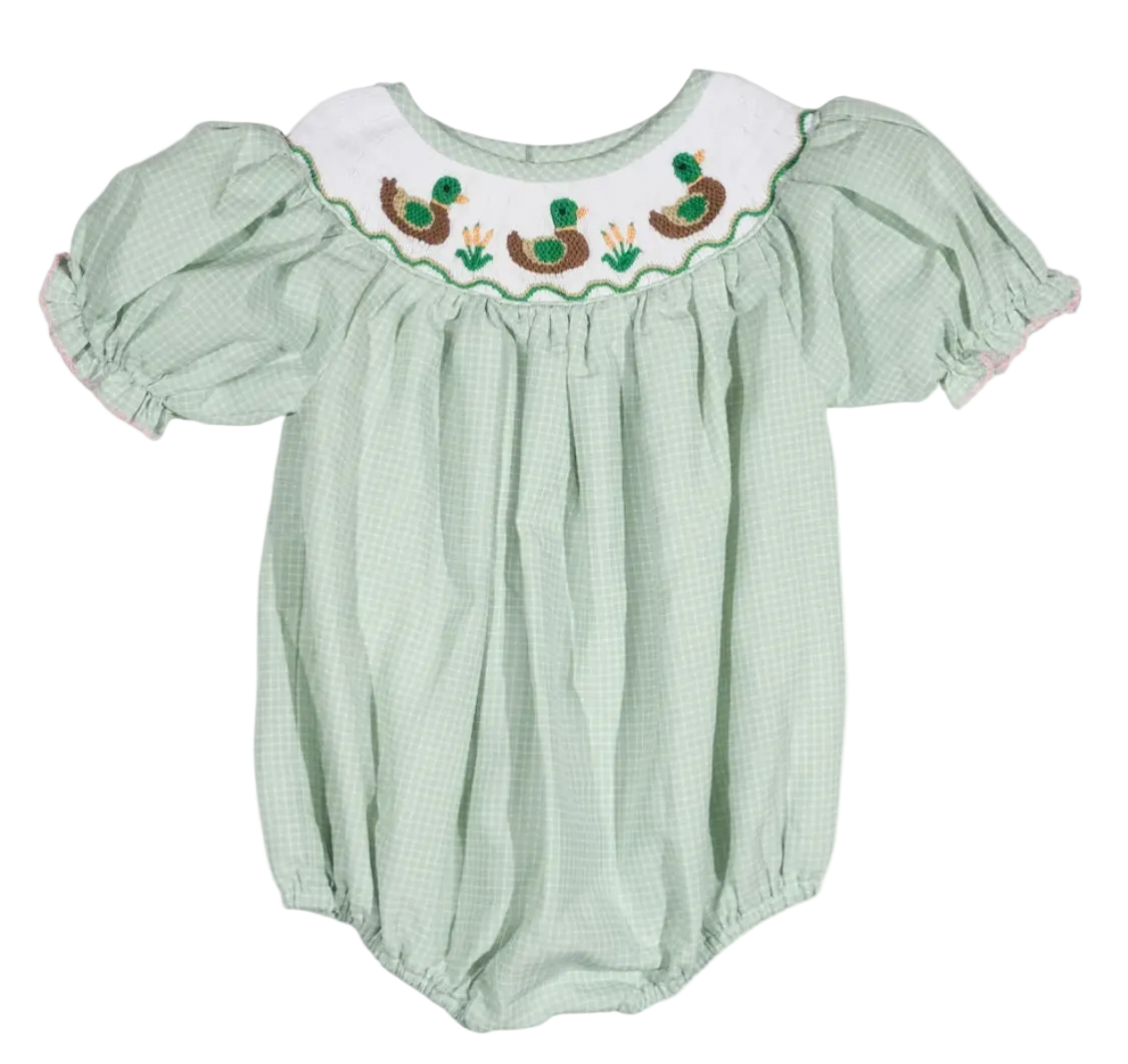 A baby bubble romper in a light green and white gingham pattern, featuring a white smocked yoke with embroidered ducks and green grass.