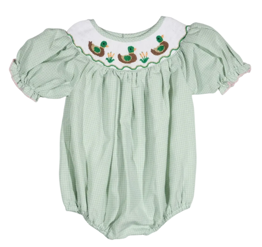 A baby bubble romper in a light green and white gingham pattern, featuring a white smocked yoke with embroidered ducks and green grass.