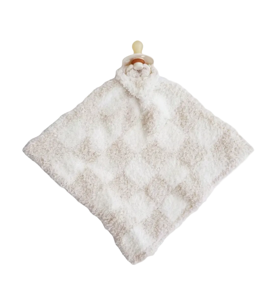 A soft, textured baby security blanket in a warm off-white or cream color, featuring a diamond pattern and a pacifier clip with a beige pacifier on a solid white background.