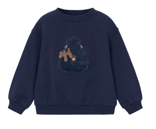 A navy blue crewneck sweatshirt featuring a plush, textured applique of a dark blue handbag with a brown puzzle-shaped charm on the front, displayed against a light gray background.