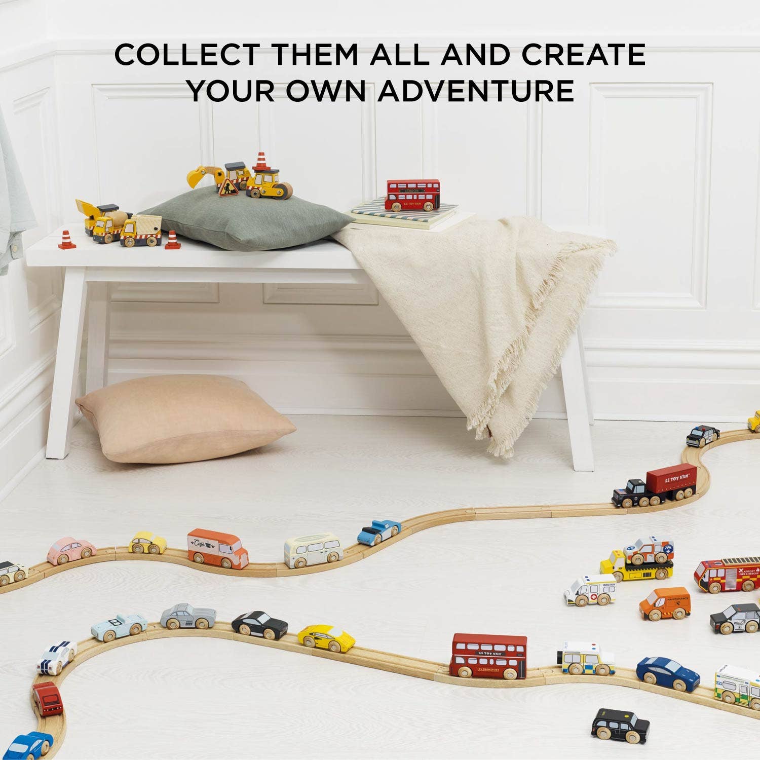 Classic Wooden Sports Cars by Le Toy Van, Inc. are displayed on a winding wooden track. Behind them, a cozy bench with cushions and a beige throw rests against a white wall.